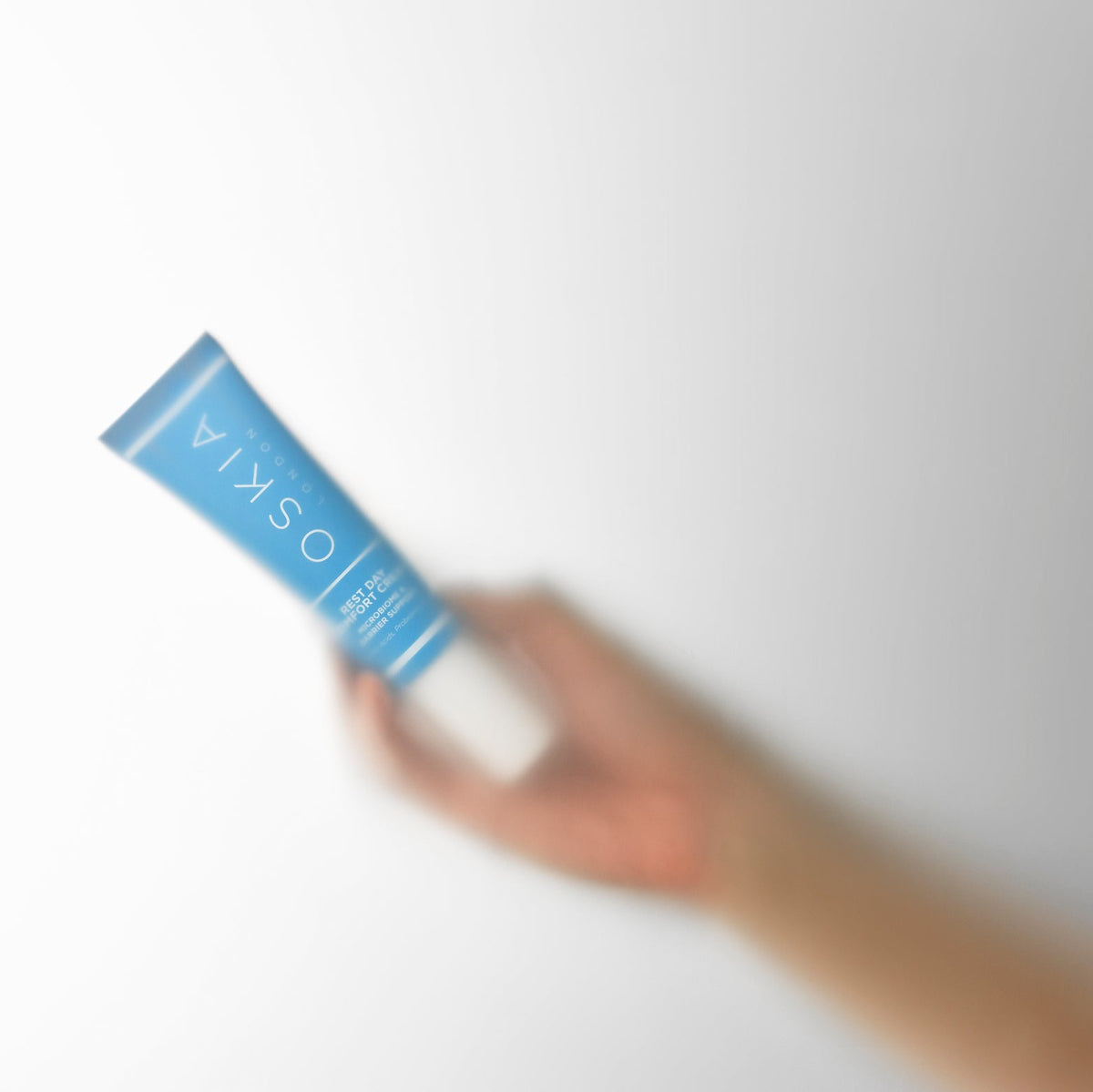 A hand holding a blue tube of OSKIA hand cream against a plain white background.
